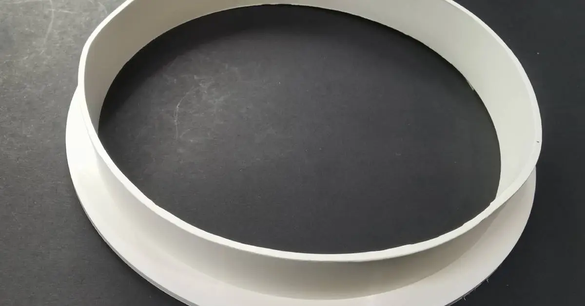 Closeup of a large circular gasket that is white and made of nitrile rubber laying on top of a black surface.