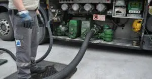 Closeup of a man standing next to the bottom loading and vapor recovery system of a tank truck with hoses attached to it.