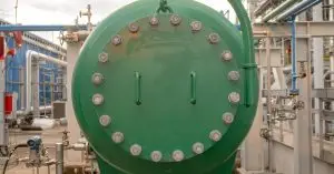 Close-up of a green tank manway gasket with bolts all around it. The tank is in an industrial setting.